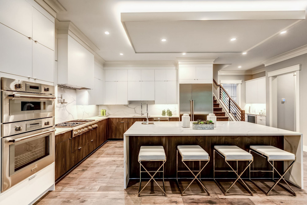 This is an example of a contemporary l-shaped kitchen in DC Metro with an undermount sink, flat-panel cabinets, white cabinets, white splashback, stone slab splashback, stainless steel appliances, medium hardwood floors, with island, brown floor, white benchtop and recessed.