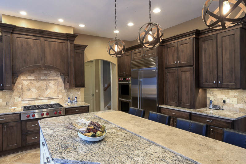 Inspiration for a large rustic u-shaped travertine floor eat-in kitchen remodel in Cleveland with a farmhouse sink, recessed-panel cabinets, dark wood cabinets, granite countertops, stone tile backsplash, stainless steel appliances, an island, beige backsplash and beige countertops
