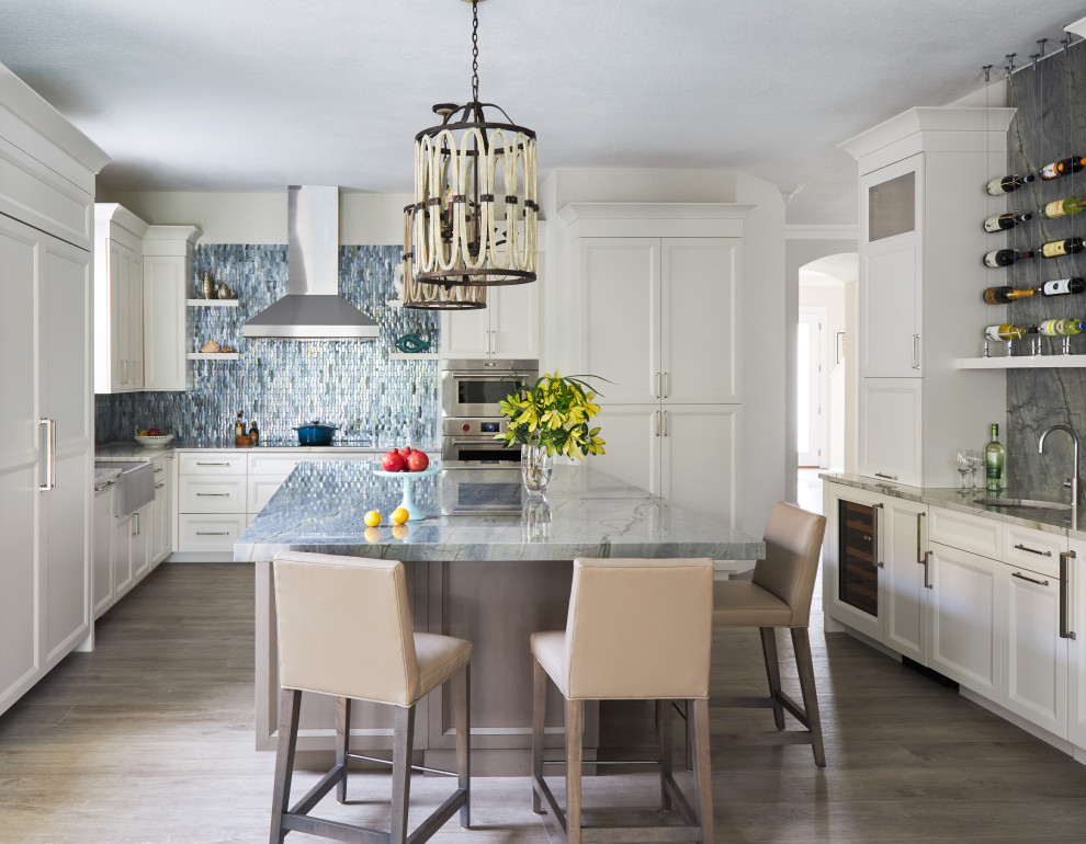 Inspiration for a large coastal l-shaped porcelain tile and gray floor kitchen remodel in Other with a farmhouse sink, recessed-panel cabinets, white cabinets, quartzite countertops, multicolored backsplash, glass tile backsplash, stainless steel appliances, an island and blue countertops