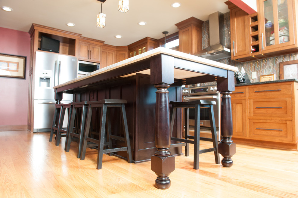 Example of a mid-sized transitional l-shaped medium tone wood floor eat-in kitchen design in Orange County with a farmhouse sink, shaker cabinets, medium tone wood cabinets, granite countertops, multicolored backsplash, matchstick tile backsplash, stainless steel appliances and an island