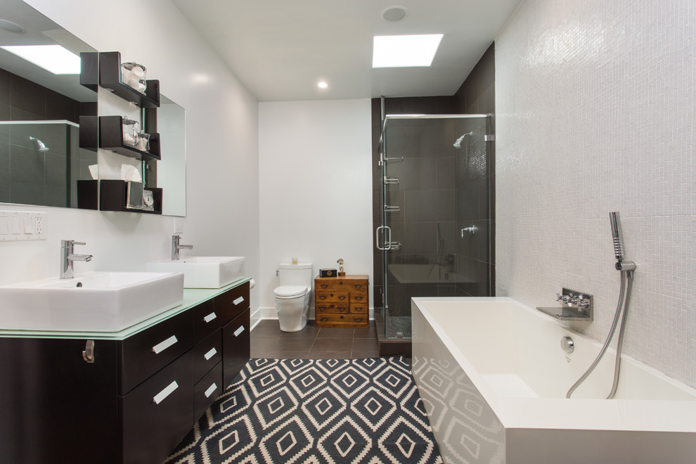 Photo of a mid-sized contemporary master bathroom in Los Angeles with dark wood cabinets, a freestanding tub, a corner shower, a one-piece toilet, white tile, black tile, white walls, ceramic floors, a wall-mount sink, glass benchtops, brown floor, a hinged shower door, flat-panel cabinets and green benchtops.