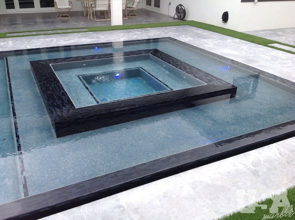 Photo of a mid-sized modern backyard rectangular infinity pool in Miami with a hot tub and natural stone pavers.