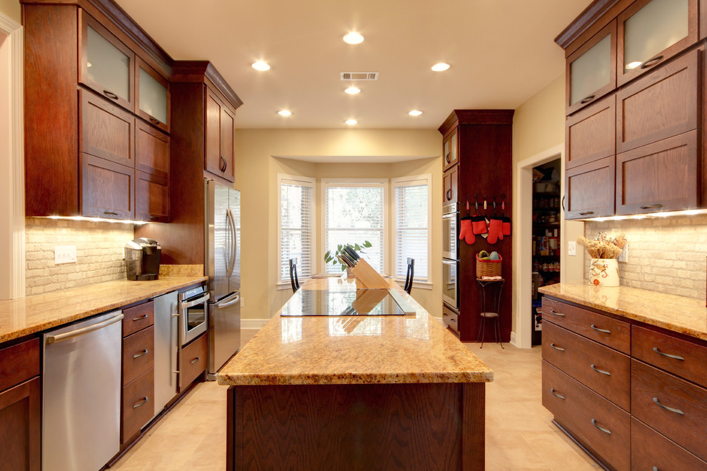 Example of a transitional eat-in kitchen design in Miami with an undermount sink, shaker cabinets, brown cabinets, granite countertops, beige backsplash, stone tile backsplash and stainless steel appliances