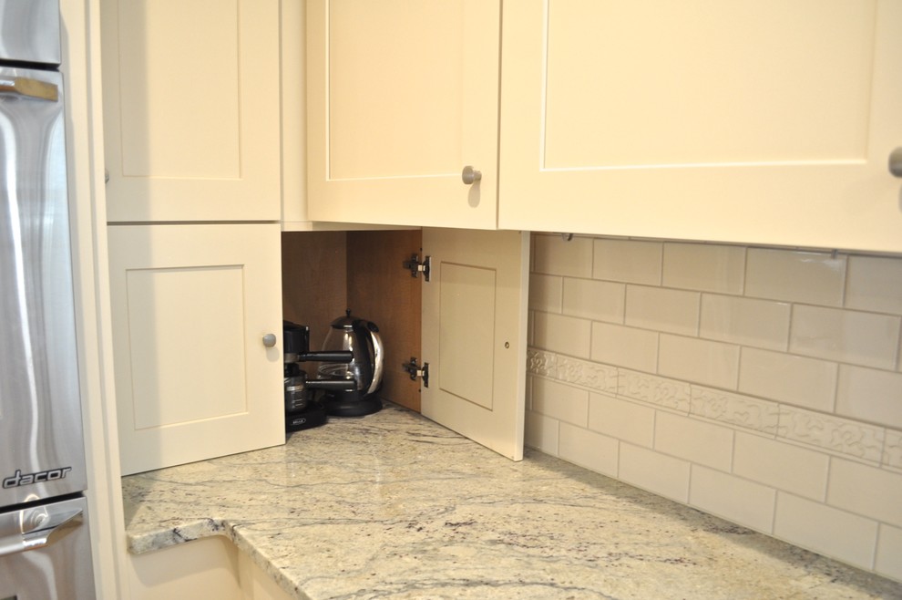 Enclosed kitchen - mid-sized transitional l-shaped light wood floor and brown floor enclosed kitchen idea in Denver with a farmhouse sink, shaker cabinets, white backsplash, ceramic backsplash, an island, white cabinets, marble countertops and stainless steel appliances