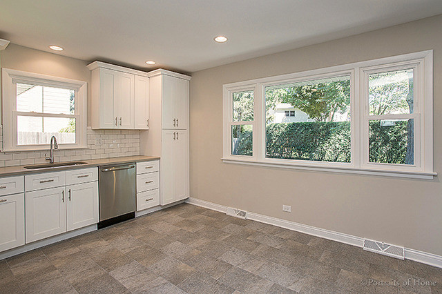 Inspiration for a mid-sized transitional l-shaped gray floor open concept kitchen remodel in Chicago with an undermount sink, shaker cabinets, white cabinets, white backsplash, subway tile backsplash, stainless steel appliances and no island