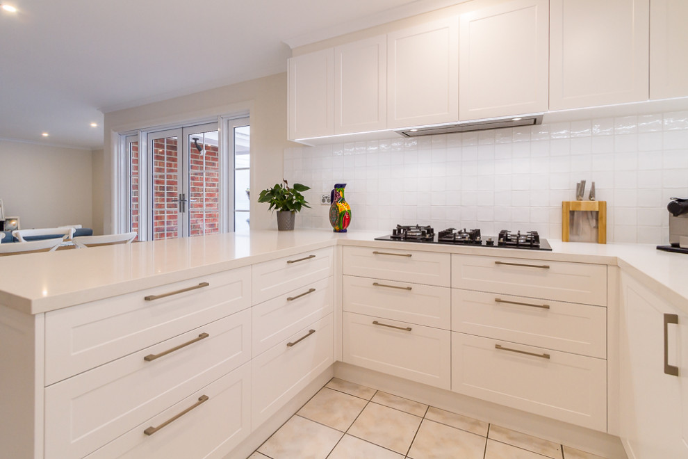 Design ideas for a mid-sized traditional u-shaped eat-in kitchen in Melbourne with a double-bowl sink, shaker cabinets, white cabinets, quartz benchtops, white splashback, porcelain splashback, stainless steel appliances, porcelain floors, a peninsula, beige floor and white benchtop.