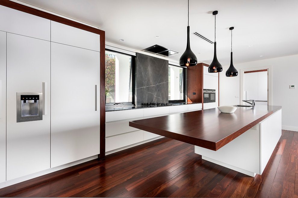 Inspiration for a large contemporary galley open plan kitchen in Perth with an undermount sink, flat-panel cabinets, white cabinets, marble benchtops, grey splashback, marble splashback, black appliances, medium hardwood floors, with island, grey floor and grey benchtop.