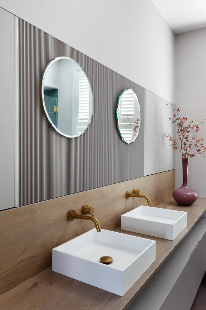 Inspiration for a medium sized contemporary bathroom in London with flat-panel cabinets, grey cabinets, a freestanding bath, a built-in shower, a wall mounted toilet, green tiles, ceramic tiles, pink walls, concrete flooring, a trough sink, wooden worktops, grey floors, a hinged door, double sinks and a floating vanity unit.