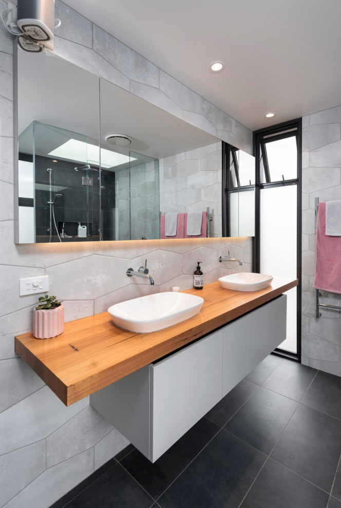 Photo of a mid-sized contemporary master bathroom in Melbourne with grey cabinets, a freestanding tub, a double shower, a two-piece toilet, white tile, porcelain tile, white walls, porcelain floors, a vessel sink, wood benchtops, grey floor and flat-panel cabinets.