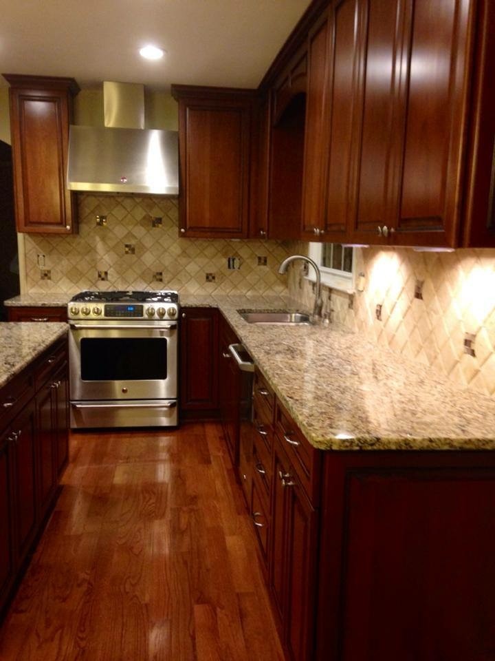 Enclosed kitchen - mid-sized transitional l-shaped medium tone wood floor and beige floor enclosed kitchen idea with a double-bowl sink, raised-panel cabinets, medium tone wood cabinets, granite countertops, beige backsplash, stone tile backsplash, stainless steel appliances and an island