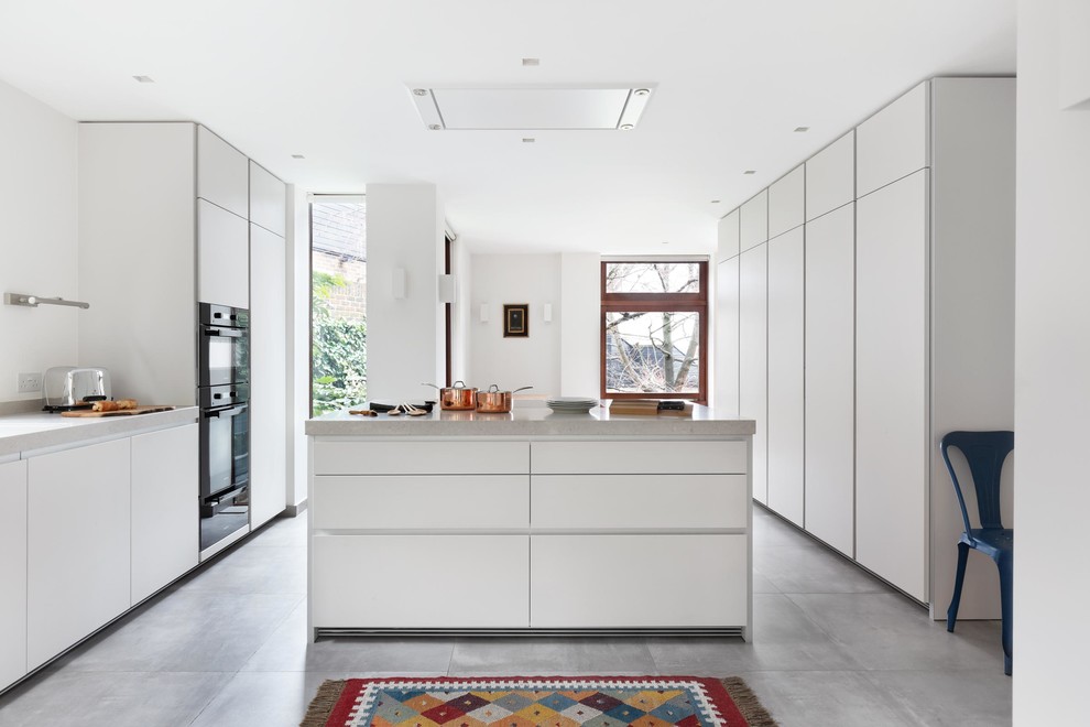 Inspiration for a mid-sized contemporary galley open plan kitchen in London with flat-panel cabinets, white cabinets, quartz benchtops, white splashback, black appliances, ceramic floors and with island.