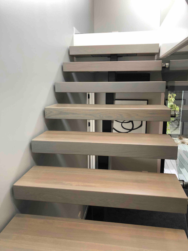 This is an example of a small modern wood floating staircase in Auckland with open risers and glass railing.