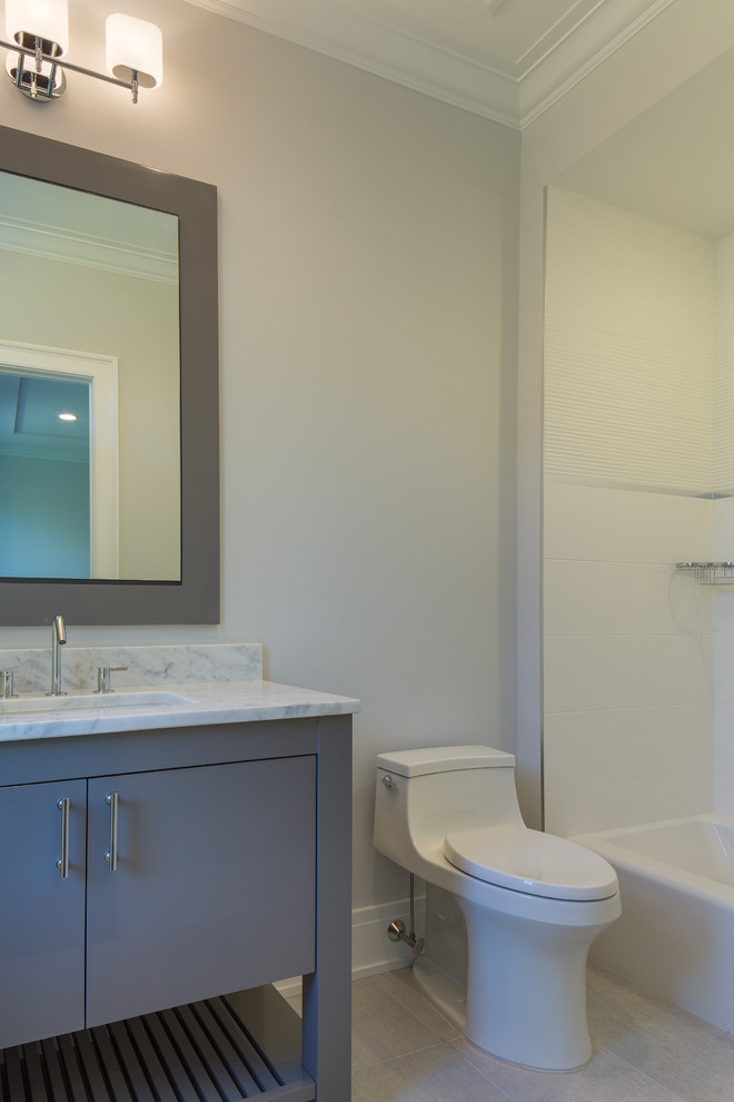 This is an example of a mid-sized transitional 3/4 bathroom in New York with flat-panel cabinets, grey cabinets, an alcove tub, a shower/bathtub combo, a one-piece toilet, grey walls, porcelain floors, an undermount sink and marble benchtops.