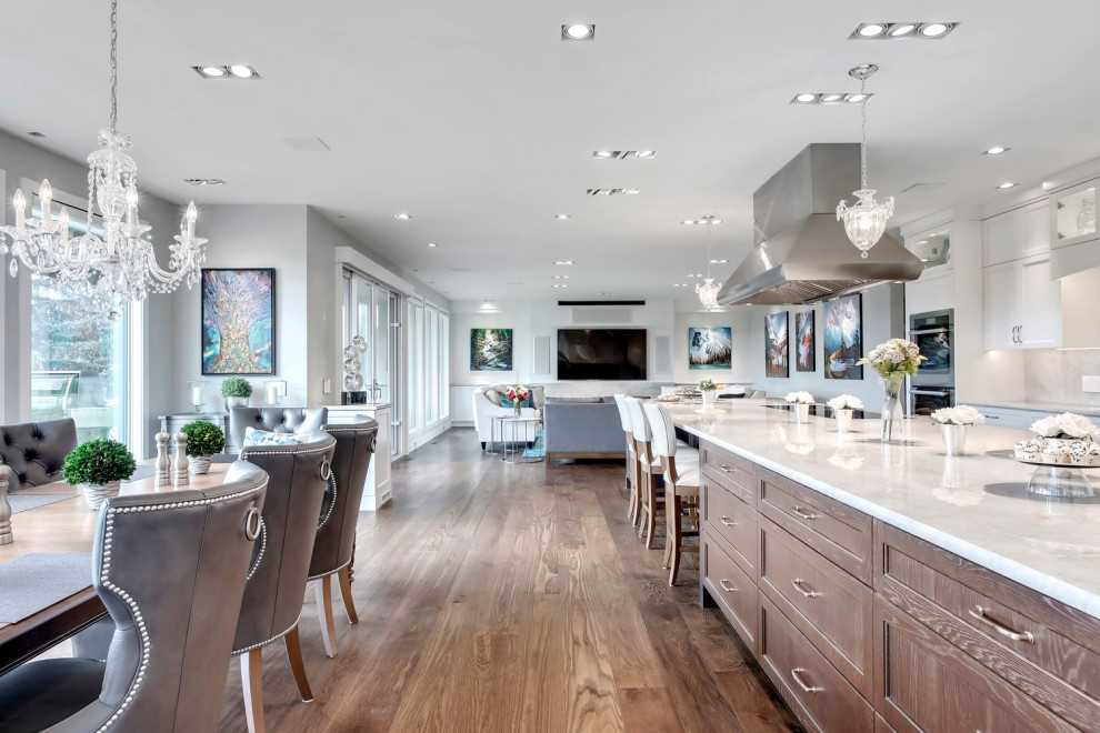 Photo of a large transitional u-shaped eat-in kitchen in Calgary with an undermount sink, recessed-panel cabinets, white cabinets, marble benchtops, white splashback, stone slab splashback, stainless steel appliances, medium hardwood floors, with island, brown floor and white benchtop.