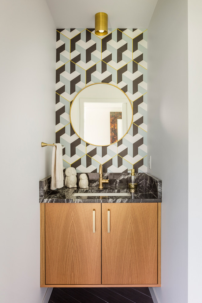 Design ideas for a midcentury powder room in Kansas City with flat-panel cabinets, medium wood cabinets, multi-coloured walls, an undermount sink, brown floor and black benchtops.