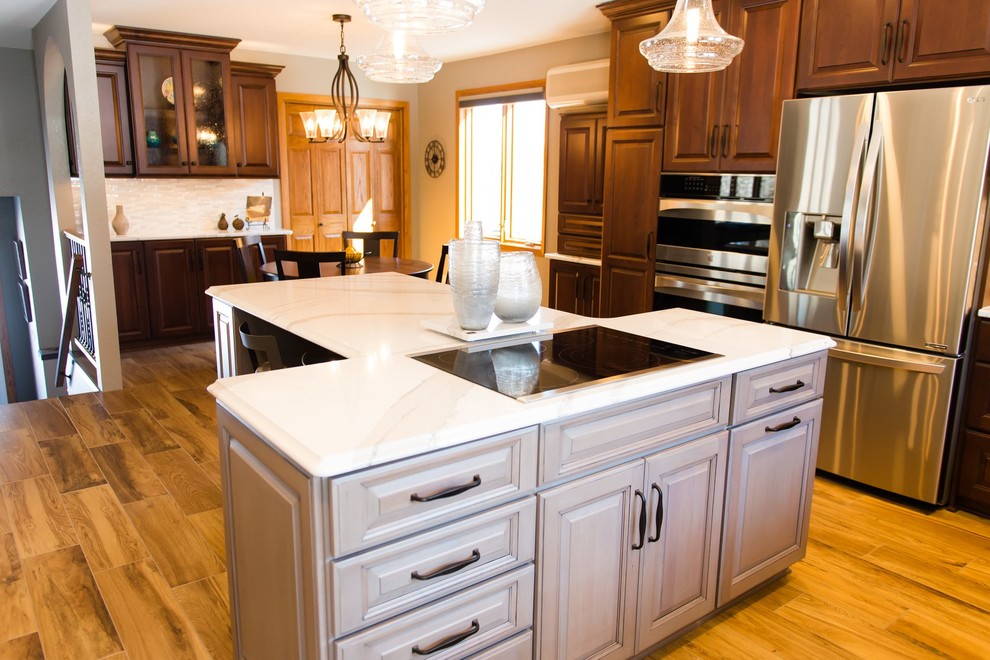 Mid-sized transitional ceramic tile and brown floor eat-in kitchen photo with white cabinets, quartzite countertops, beige backsplash, ceramic backsplash, stainless steel appliances, an island and white countertops