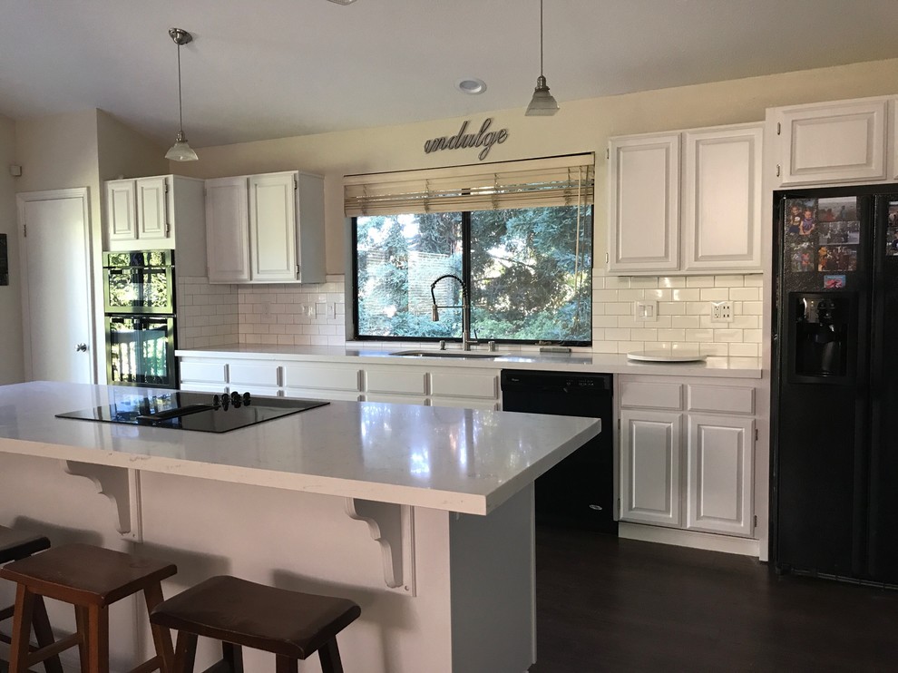 Mid-sized country eat-in kitchen in Other with an undermount sink, flat-panel cabinets, white cabinets, marble benchtops, white splashback, subway tile splashback, black appliances, laminate floors, with island and brown floor.
