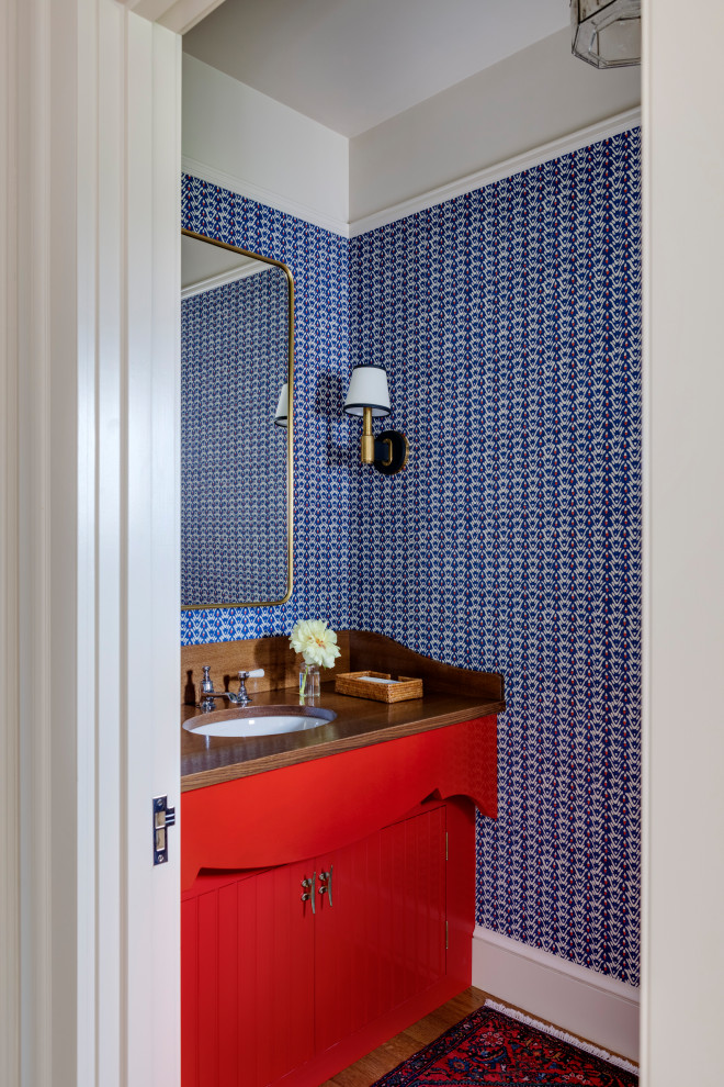 Small beach style medium tone wood floor and wallpaper powder room photo in Boston with red cabinets, blue walls, wood countertops, brown countertops and a built-in vanity