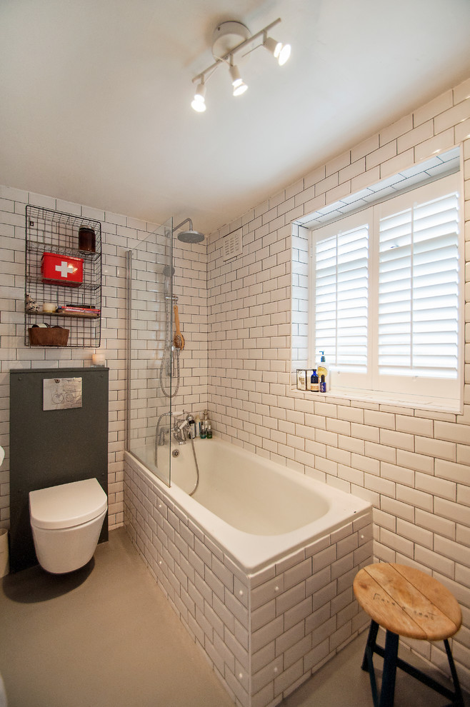 Inspiration for an eclectic bathroom in London with a shower/bathtub combo, a wall-mount toilet, white tile, subway tile and a drop-in tub.