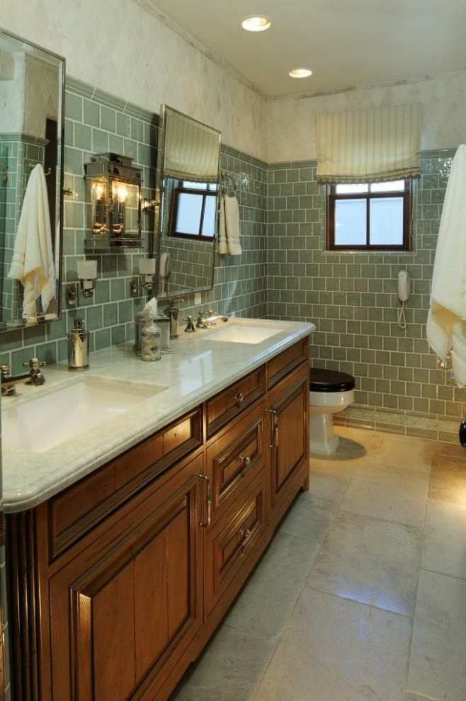 This is an example of a mid-sized 3/4 bathroom in Los Angeles with furniture-like cabinets, medium wood cabinets, an alcove shower, a two-piece toilet, white tile, subway tile, green walls, limestone floors, an undermount sink, engineered quartz benchtops, beige floor, a hinged shower door, white benchtops, a shower seat, a double vanity, a freestanding vanity and wallpaper.