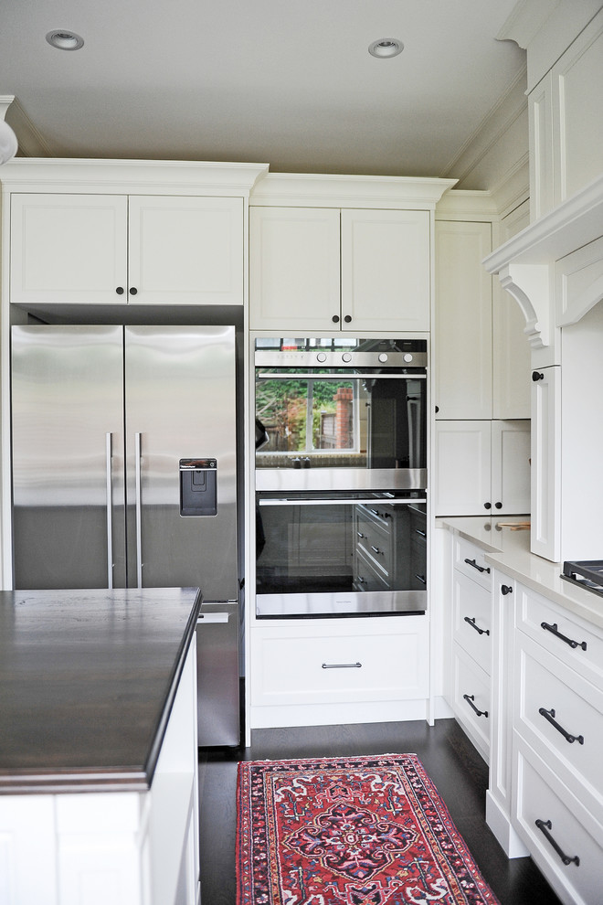 Inspiration for a mid-sized transitional u-shaped dark wood floor enclosed kitchen remodel in Vancouver with an undermount sink, recessed-panel cabinets, white cabinets, wood countertops, beige backsplash, terra-cotta backsplash, stainless steel appliances and an island