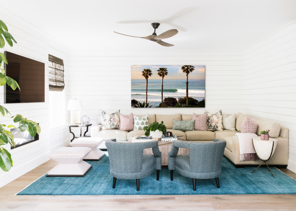 Photo of a beach style open concept family room in San Diego with white walls, light hardwood floors, a ribbon fireplace, a wood fireplace surround, a wall-mounted tv, beige floor and planked wall panelling.