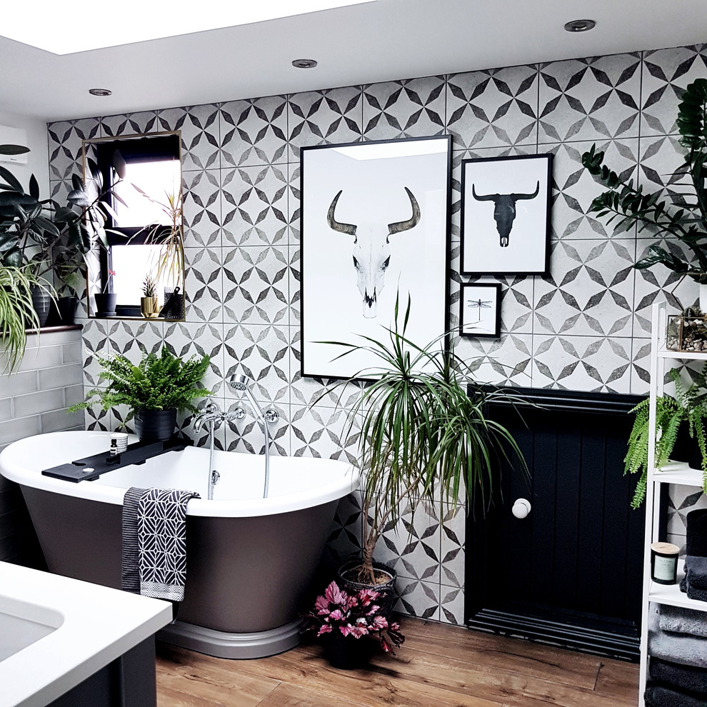 Scandinavian master bathroom with a freestanding tub, black and white tile, gray tile, medium hardwood floors and brown floor.