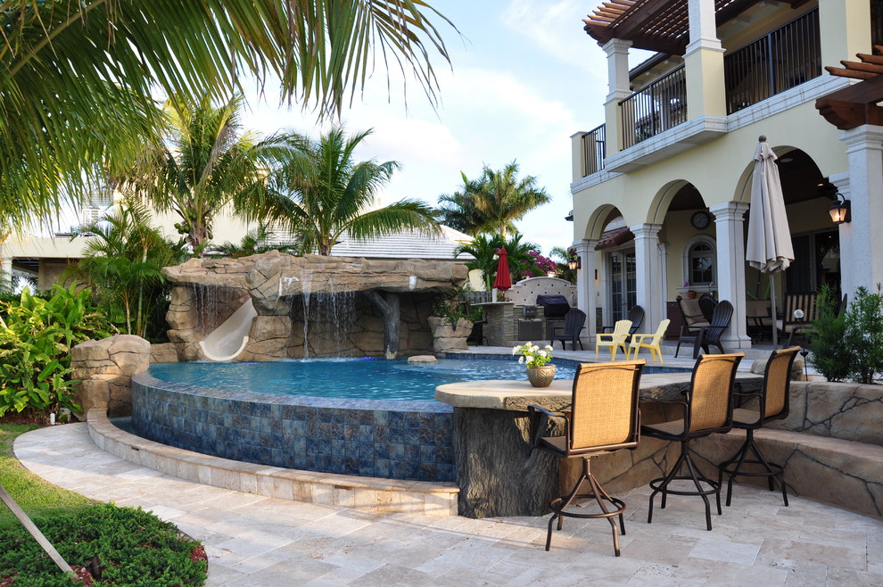 Inspiration for a mediterranean custom-shaped pool in Miami with natural stone pavers and a water slide.