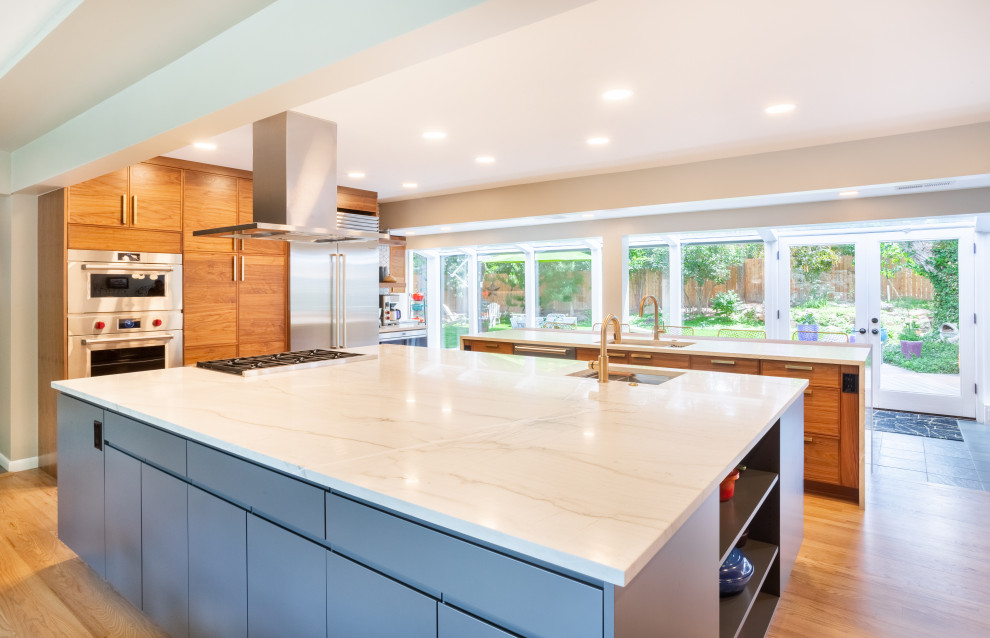 This is an example of a large midcentury single-wall eat-in kitchen in Denver with an undermount sink, shaker cabinets, medium wood cabinets, quartzite benchtops, white splashback, porcelain splashback, stainless steel appliances, light hardwood floors, multiple islands, beige floor and white benchtop.