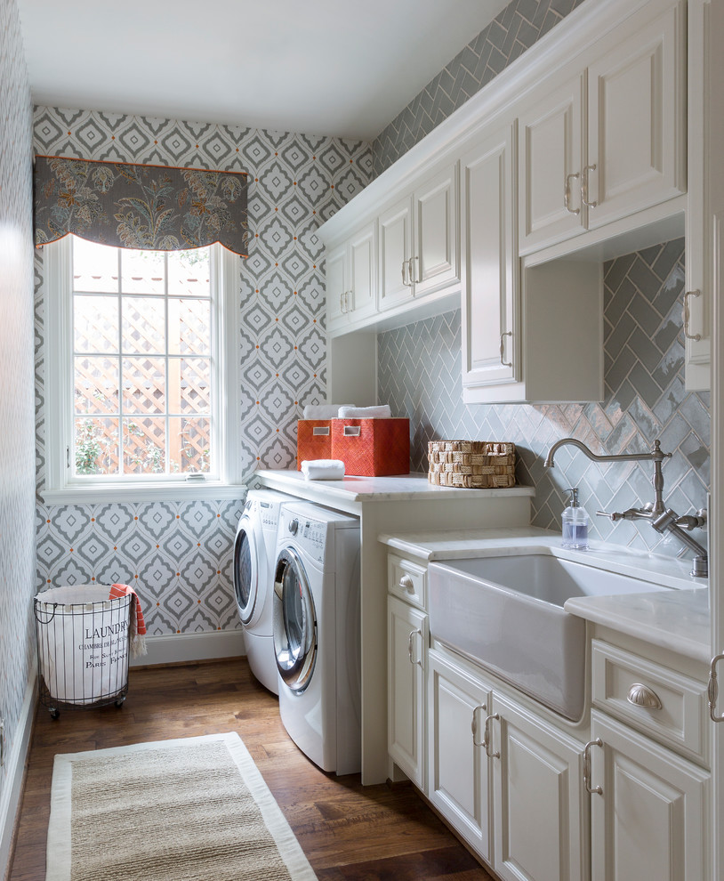 Photo of a traditional single-wall dedicated laundry room in Dallas with a farmhouse sink, raised-panel cabinets, white cabinets, multi-coloured walls, medium hardwood floors, a side-by-side washer and dryer, brown floor and white benchtop.