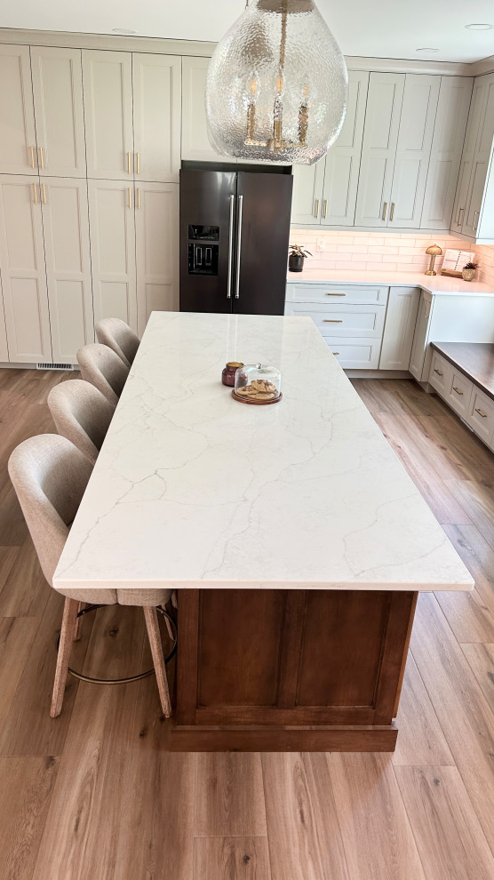 Example of a large transitional u-shaped light wood floor open concept kitchen design with an undermount sink, flat-panel cabinets, white cabinets, quartz countertops, white backsplash, ceramic backsplash, black appliances, an island and white countertops