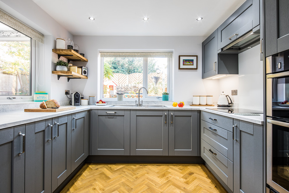 Design ideas for a mid-sized transitional u-shaped separate kitchen in Other with shaker cabinets, grey cabinets, laminate benchtops, white splashback, glass sheet splashback, panelled appliances, vinyl floors, a peninsula, brown floor, white benchtop and a drop-in sink.