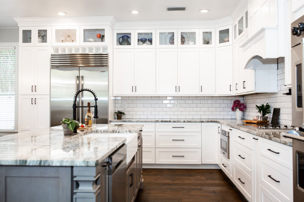 Inspiration for a modern l-shaped kitchen/diner in Tampa with a belfast sink, shaker cabinets, white cabinets, white splashback, metro tiled splashback, medium hardwood flooring, an island and brown floors.