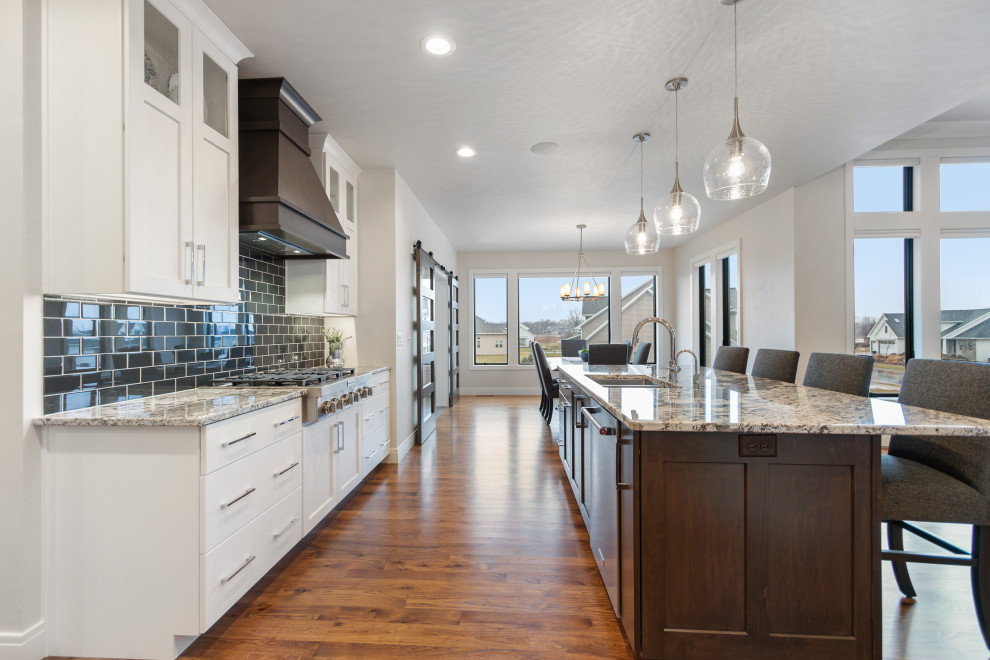 Example of a mid-sized transitional l-shaped medium tone wood floor and brown floor eat-in kitchen design with an undermount sink, shaker cabinets, white cabinets, granite countertops, blue backsplash, subway tile backsplash, stainless steel appliances, multicolored countertops and an island
