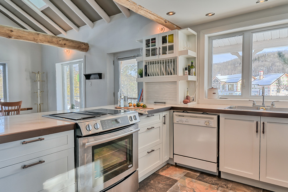 Mid-sized eclectic u-shaped eat-in kitchen in Montreal with a double-bowl sink, shaker cabinets, white cabinets, tile benchtops, white splashback, window splashback, stainless steel appliances, slate floors and a peninsula.