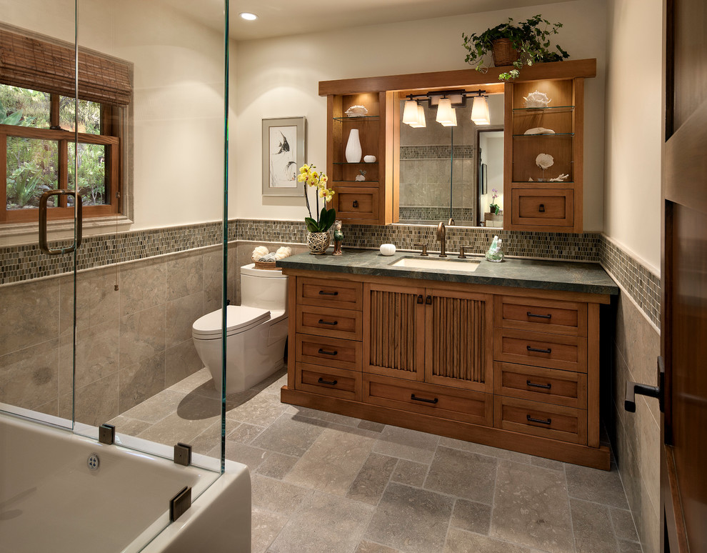 Design ideas for a mid-sized asian master bathroom in Santa Barbara with an undermount sink, furniture-like cabinets, medium wood cabinets, granite benchtops, a shower/bathtub combo, a one-piece toilet, gray tile, stone tile, white walls and limestone floors.