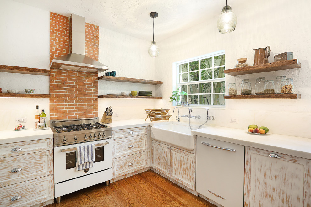 Photo of a country l-shaped kitchen in Miami with a farmhouse sink, shaker cabinets, white cabinets, orange splashback, white appliances and medium hardwood floors.