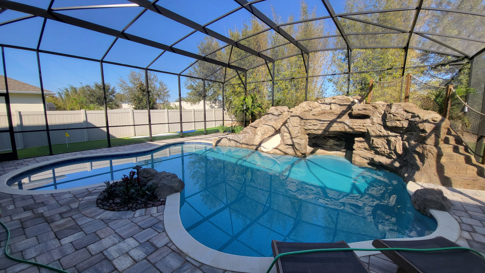Imagen de piscina con tobogán natural tropical de tamaño medio a medida en patio trasero con adoquines de ladrillo