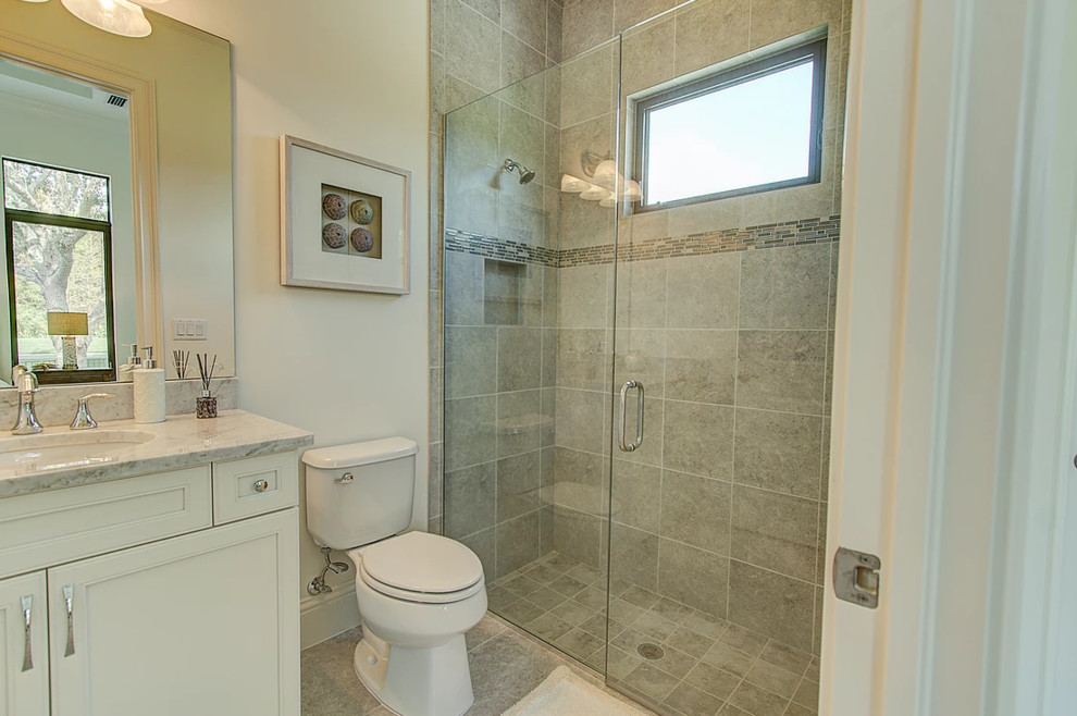 Photo of a small transitional 3/4 bathroom in Miami with recessed-panel cabinets, white cabinets, an alcove shower, a two-piece toilet, beige tile, porcelain tile, beige walls, porcelain floors, an undermount sink, marble benchtops, beige floor and a hinged shower door.