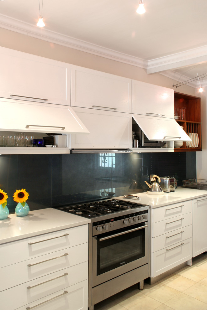 Photo of a contemporary u-shaped eat-in kitchen in Other with a double-bowl sink, shaker cabinets, white cabinets, quartz benchtops, blue splashback, glass sheet splashback and stainless steel appliances.