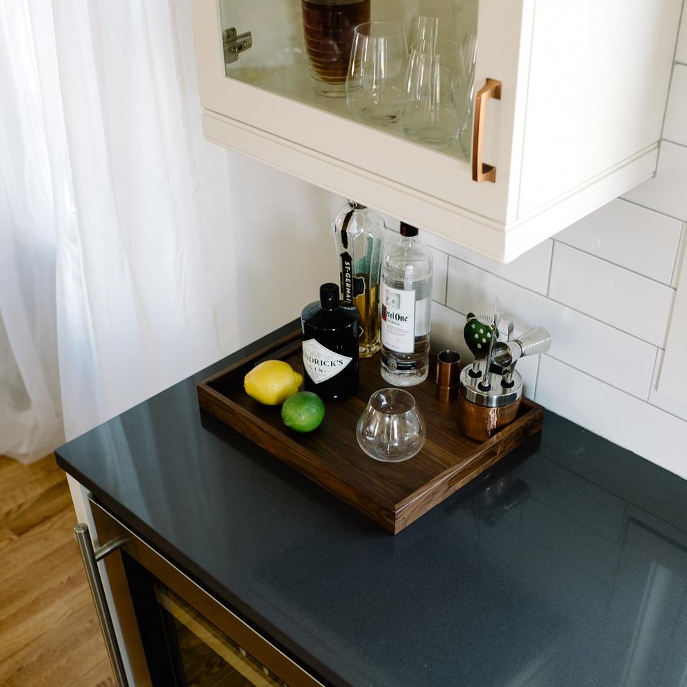 This is an example of a small home bar in Minneapolis with no sink, white cabinets, quartz benchtops, white splashback, subway tile splashback and medium hardwood floors.