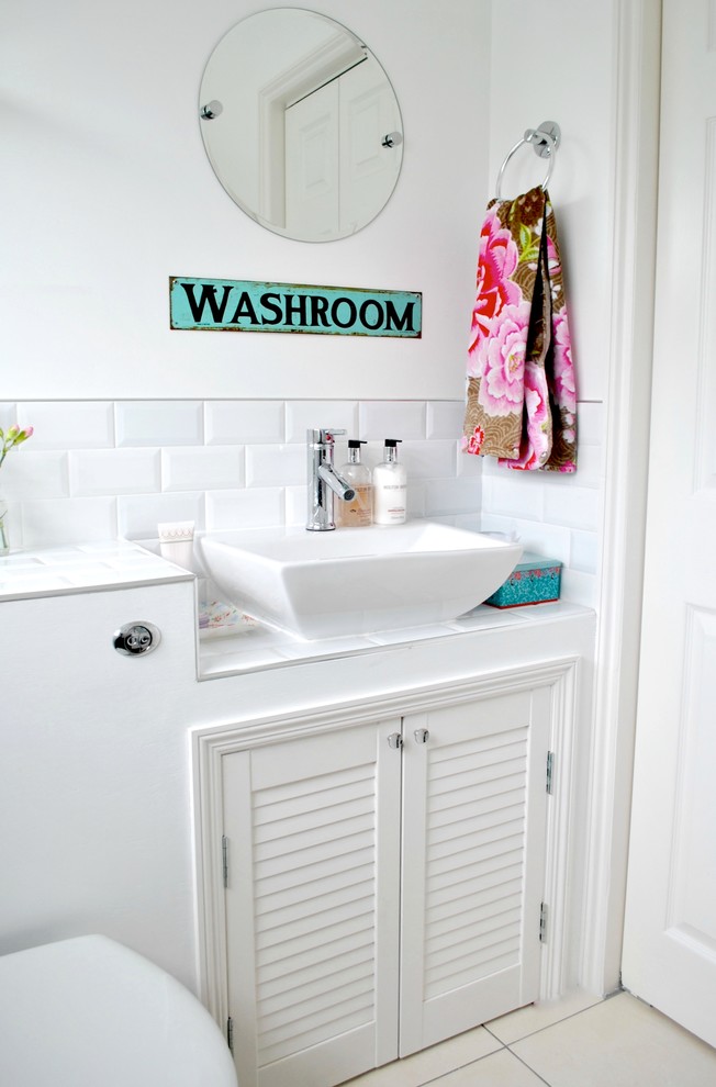 Photo of a traditional powder room in Devon with a vessel sink, louvered cabinets, white cabinets, tile benchtops, a one-piece toilet, white tile and subway tile.