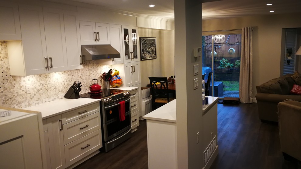 Inspiration for a mid-sized transitional galley eat-in kitchen in Vancouver with an undermount sink, shaker cabinets, white cabinets, solid surface benchtops, beige splashback, stone tile splashback, stainless steel appliances, dark hardwood floors, with island, brown floor and white benchtop.