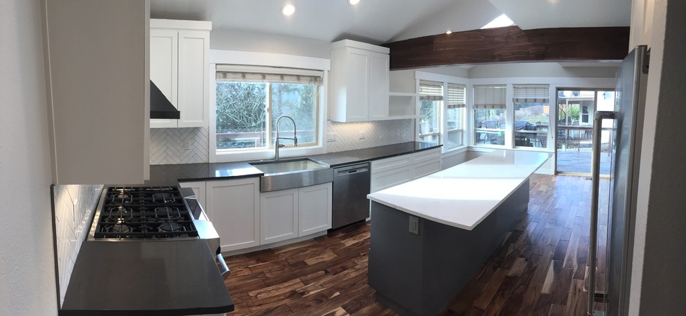 This is an example of a mid-sized transitional l-shaped eat-in kitchen in Portland with a farmhouse sink, shaker cabinets, white cabinets, quartz benchtops, white splashback, ceramic splashback, stainless steel appliances, dark hardwood floors and with island.