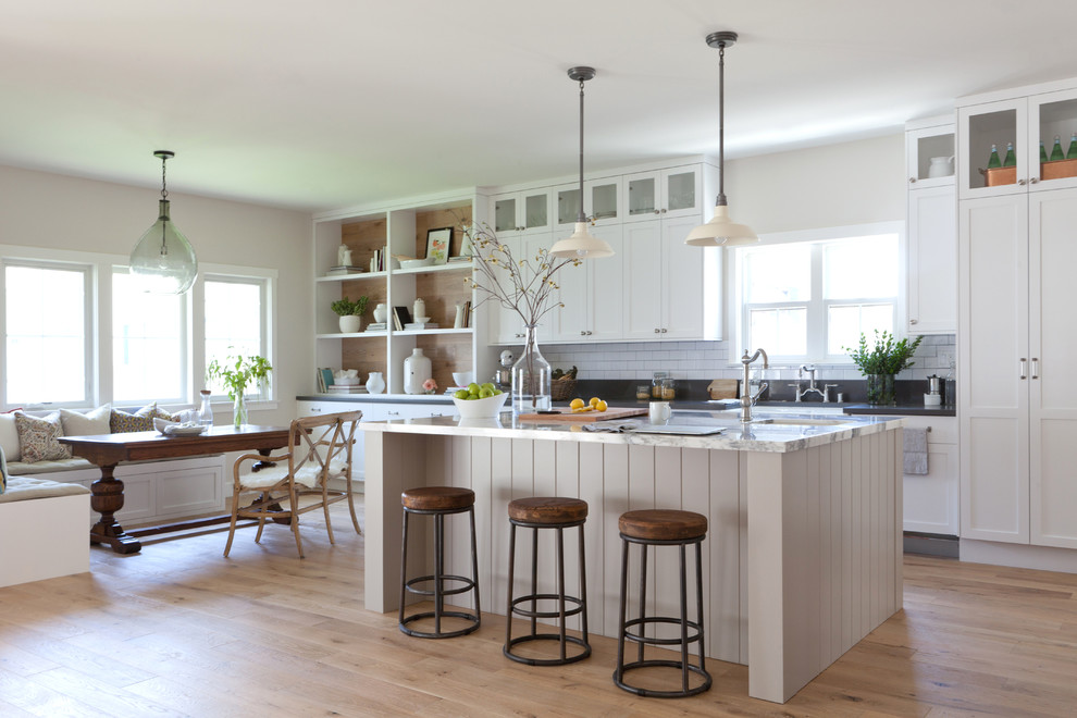 This is an example of a large country galley open plan kitchen in Los Angeles with shaker cabinets, white cabinets, marble benchtops, white splashback, medium hardwood floors, with island and subway tile splashback.