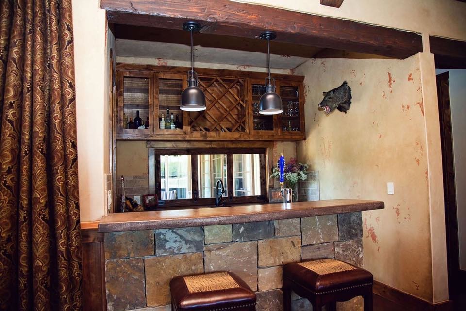Photo of a mid-sized country galley seated home bar in Austin with an undermount sink, shaker cabinets, dark wood cabinets, concrete benchtops, beige splashback, stone slab splashback, concrete floors, brown floor and grey benchtop.