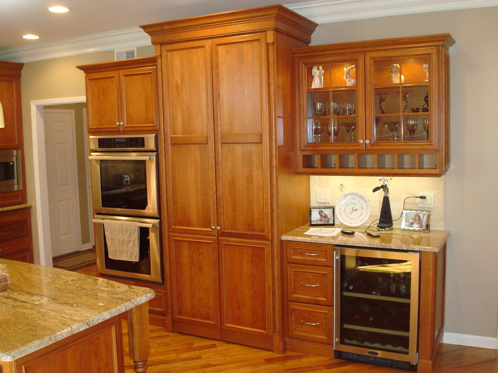 This is an example of a large traditional u-shaped eat-in kitchen in New York with a drop-in sink, beaded inset cabinets, medium wood cabinets, granite benchtops, beige splashback, stainless steel appliances, medium hardwood floors and with island.