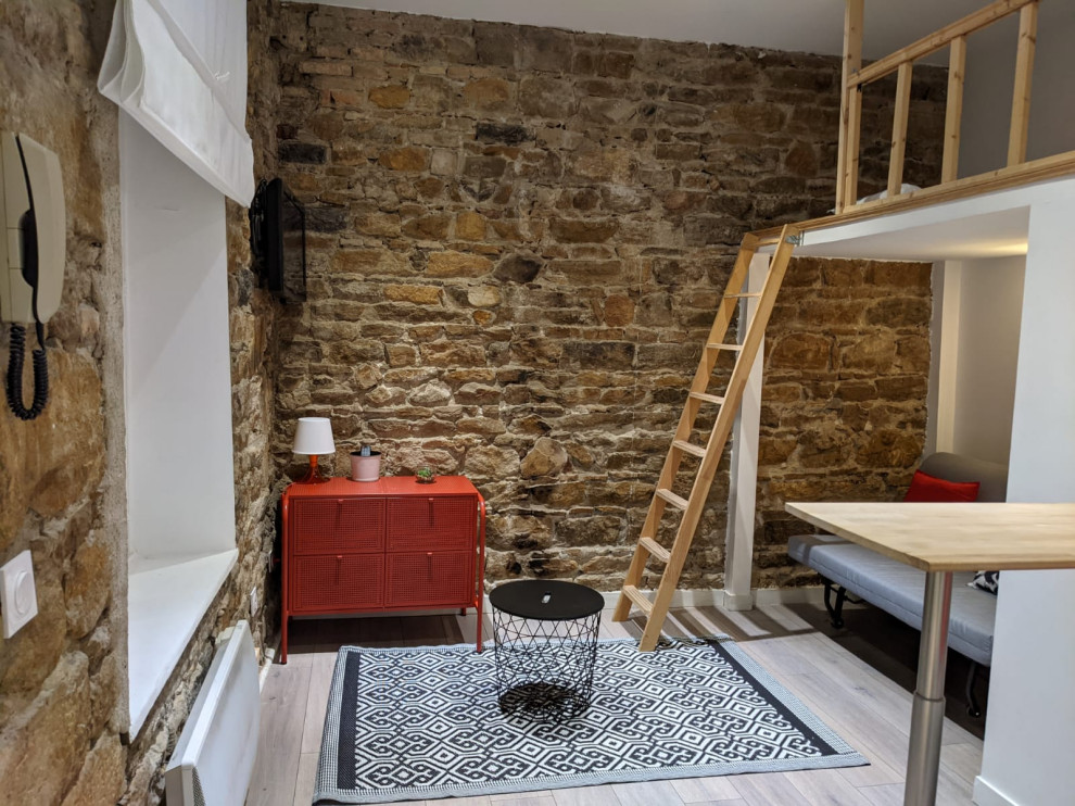Exemple d'un petit salon mansardé ou avec mezzanine tendance avec sol en stratifié, aucune cheminée, un téléviseur fixé au mur, un sol gris et un mur en pierre.