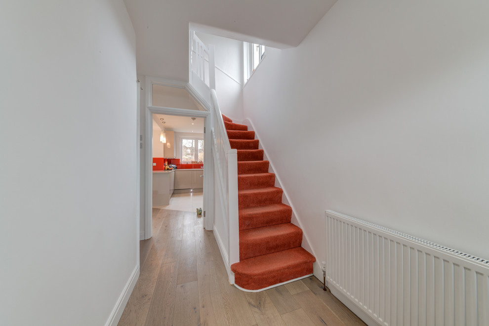 This is an example of a mid-sized modern carpeted straight staircase in London with carpet risers and wood railing.