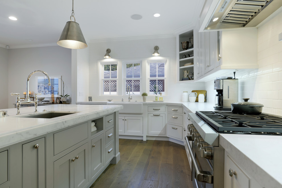 Mid-sized traditional l-shaped open plan kitchen in Los Angeles with a farmhouse sink, shaker cabinets, white cabinets, marble benchtops, white splashback, ceramic splashback, stainless steel appliances, medium hardwood floors and with island.